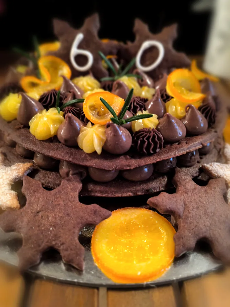 Torta al cacao a strati con ciuffi di crema, arance candite e numero sessanta